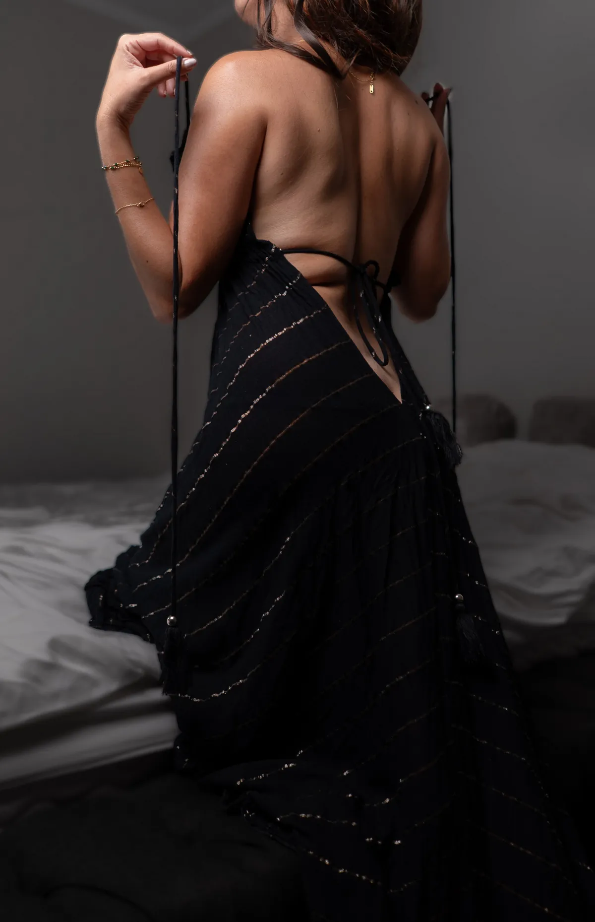Anonymous full-length boudoir portrait of a woman posing in a backless black dress