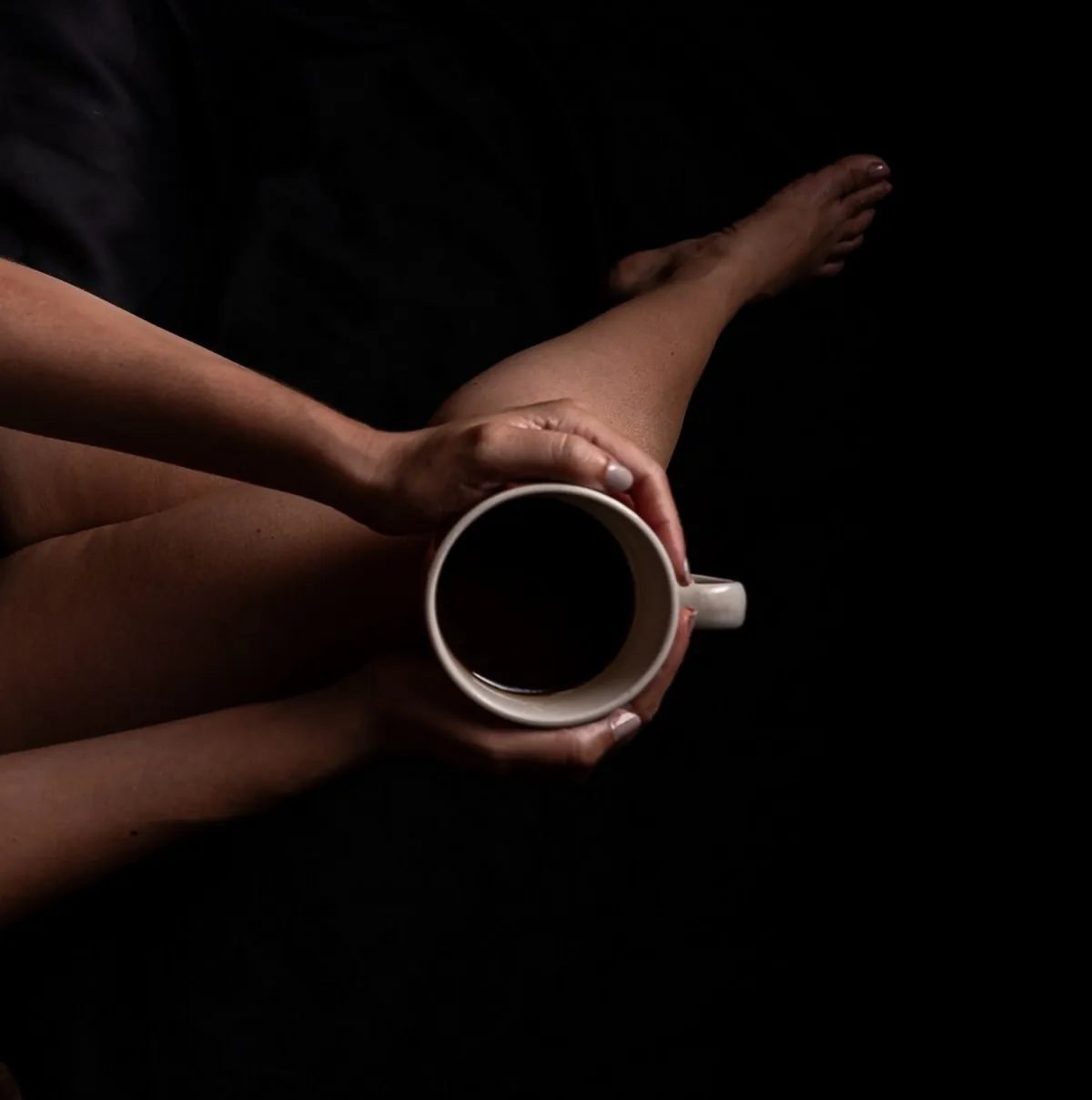 Anonymous boudoir portrait of a woman holding a coffee cup against a dark background