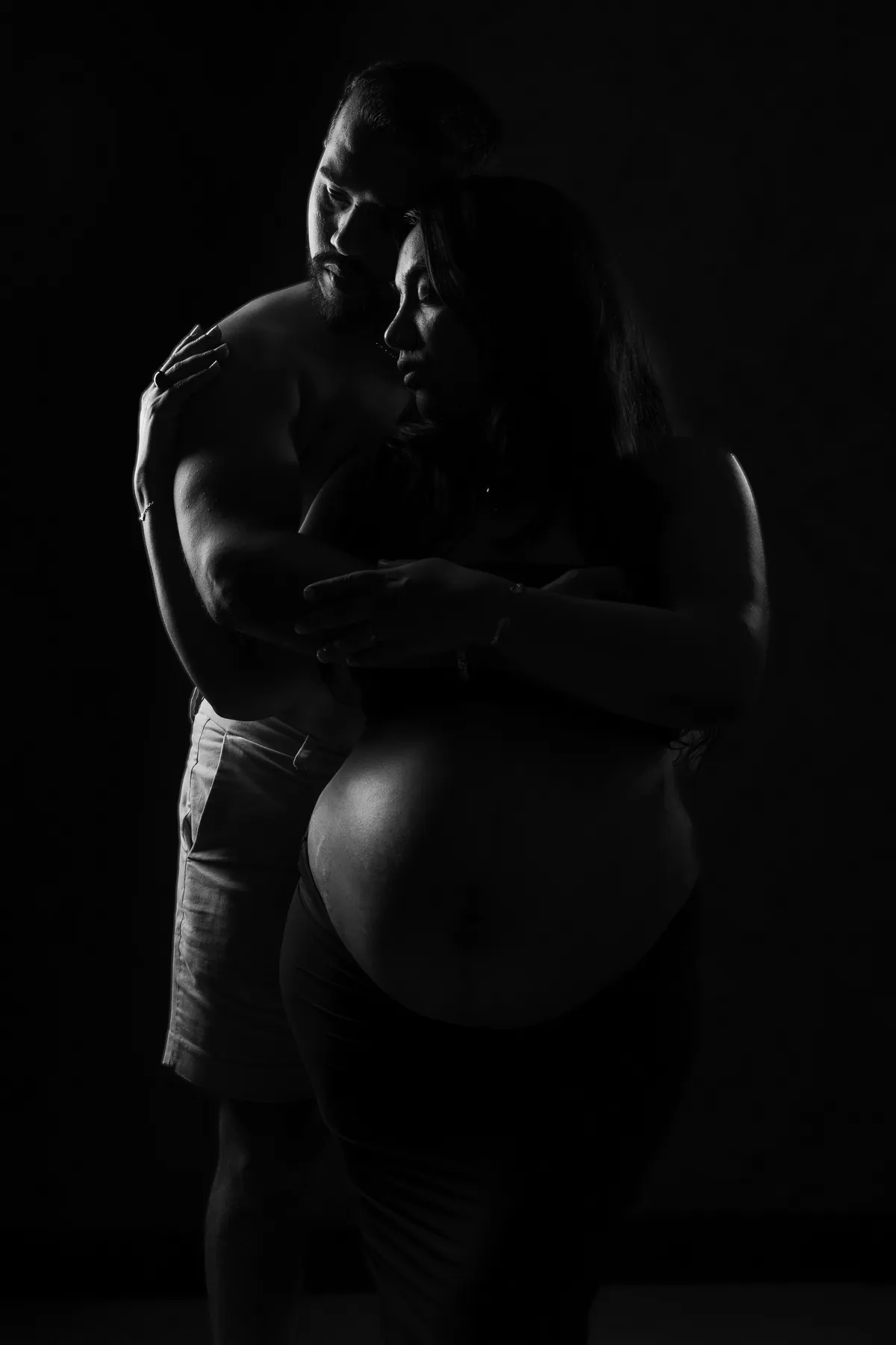 Black-and-white couple maternity portrait with a partner embracing a pregnant woman in dramatic studio light