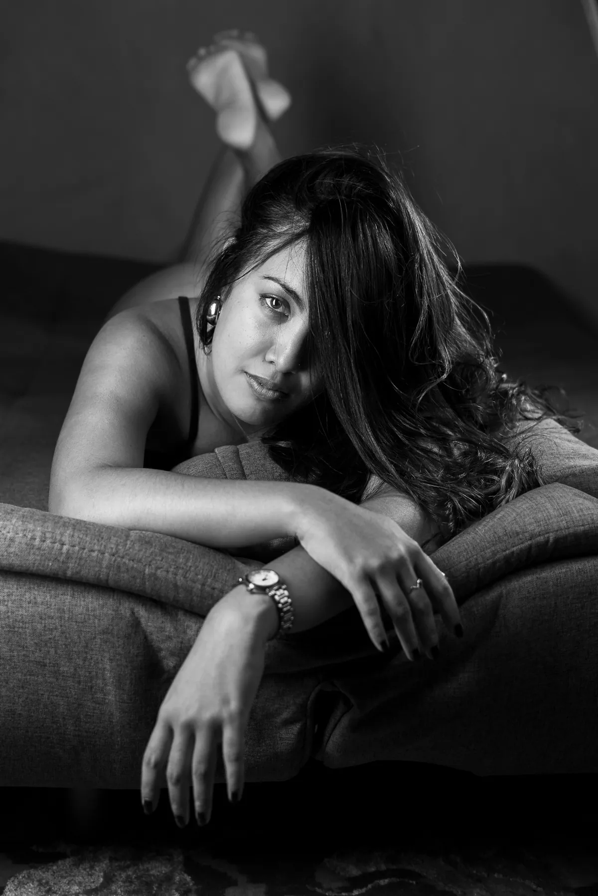 Moody black-and-white boudoir portrait of Emilie leaning across a sofa