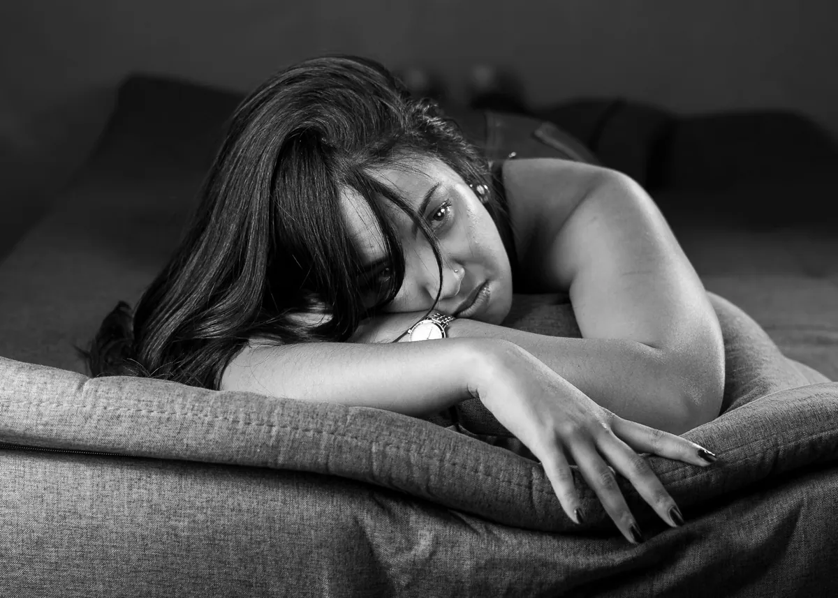 Black-and-white boudoir portrait of Emilie reclining on a sofa and looking toward the camera