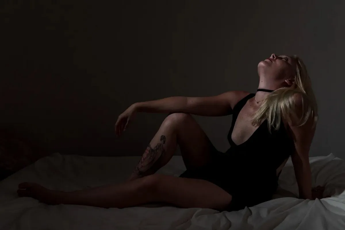 Low-key boudoir portrait of Julie reclining against a dark studio background