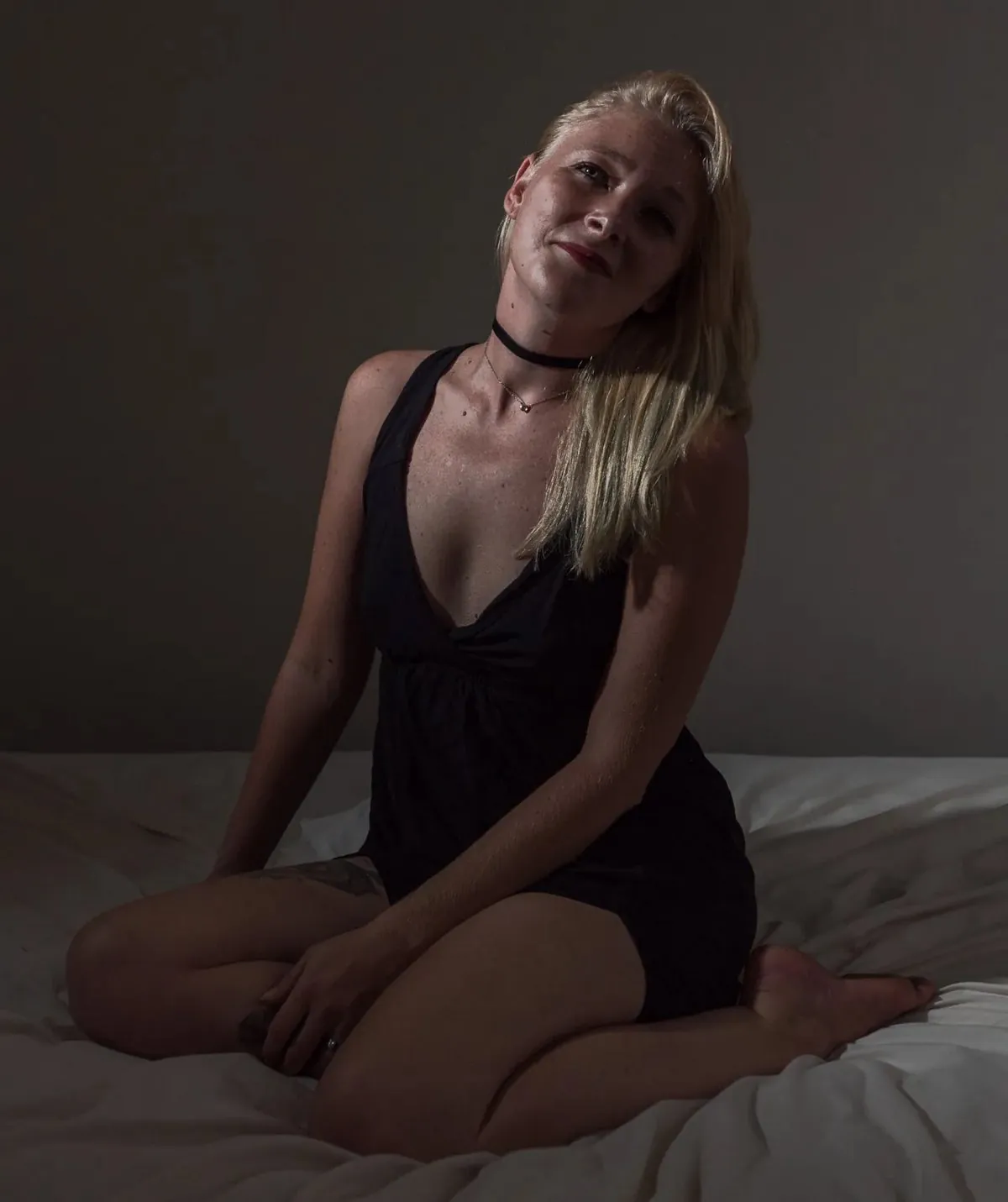 Seated boudoir portrait of Julie wearing a dark dress on a bed