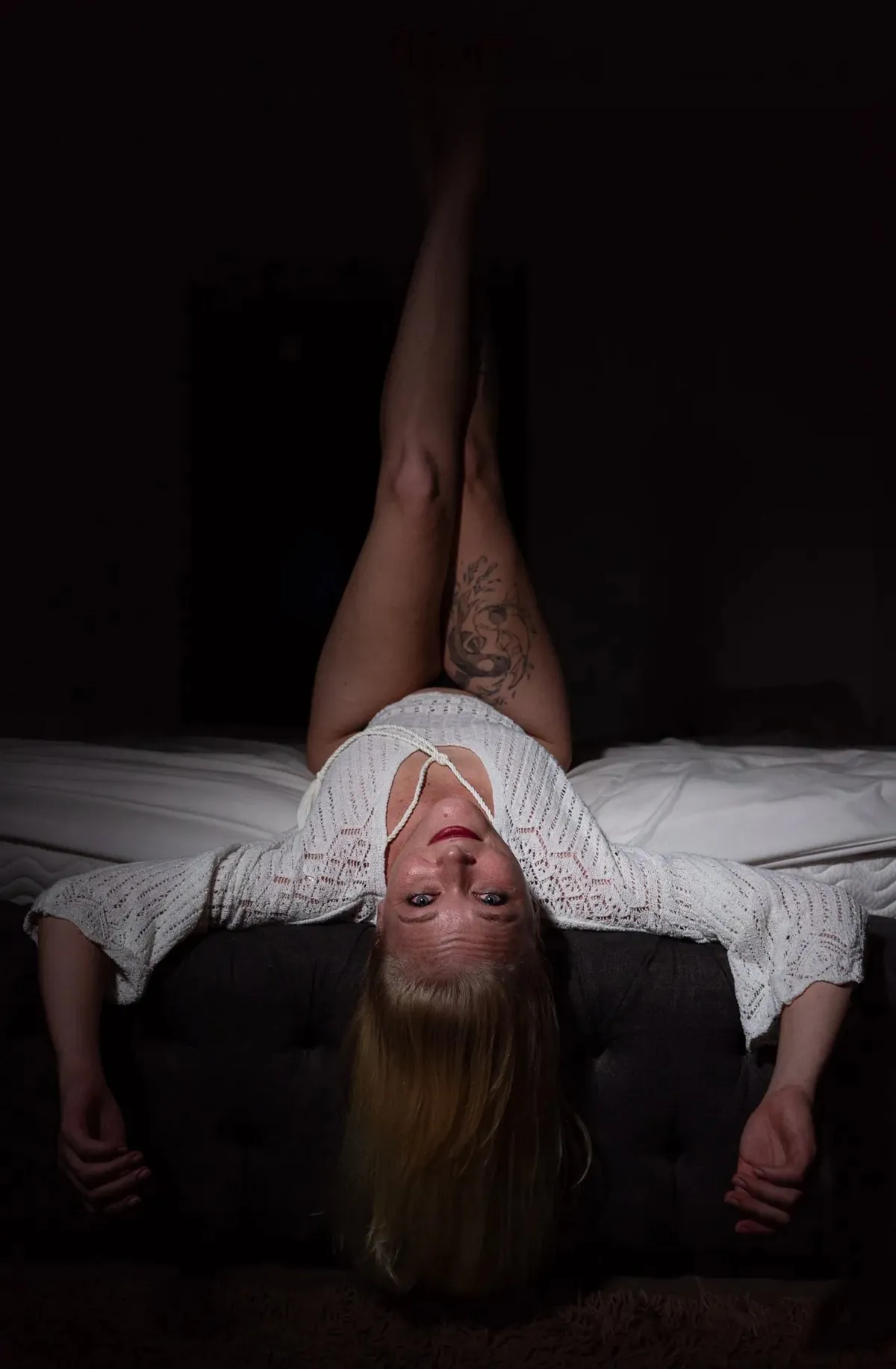 Creative boudoir portrait of Julie lying upside down on a bed with dramatic composition