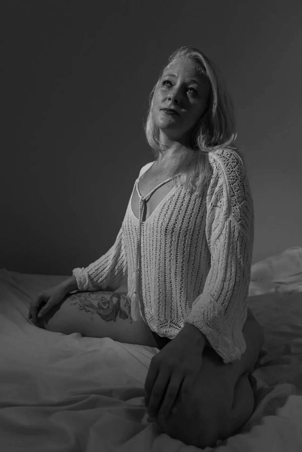 Seated black-and-white boudoir portrait of Julie wearing a white knit top
