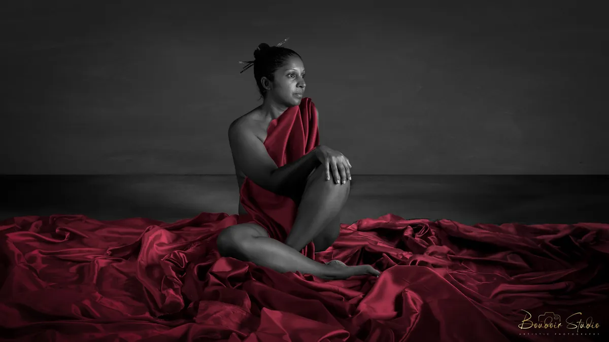 Wide creative studio portrait of Natacha Boodhoo seated among rich red fabric