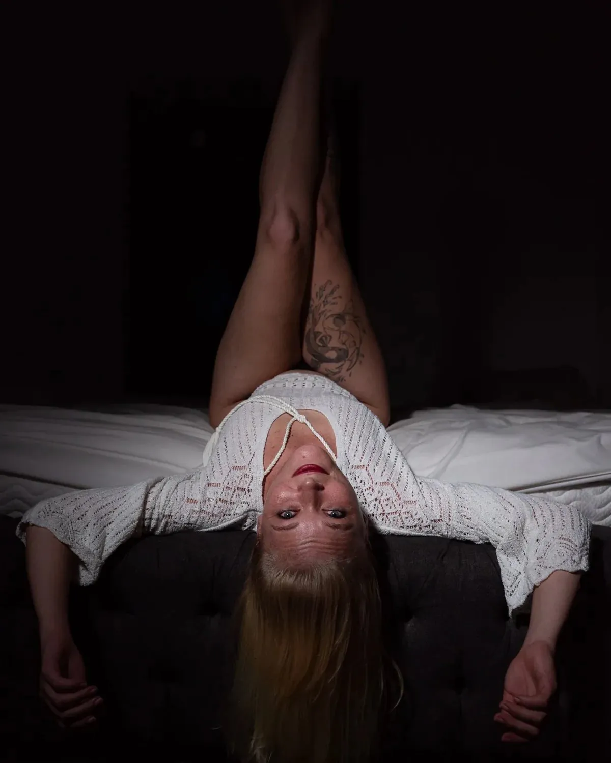 Private black-and-white boudoir portrait of a woman lying across a bed in dramatic light