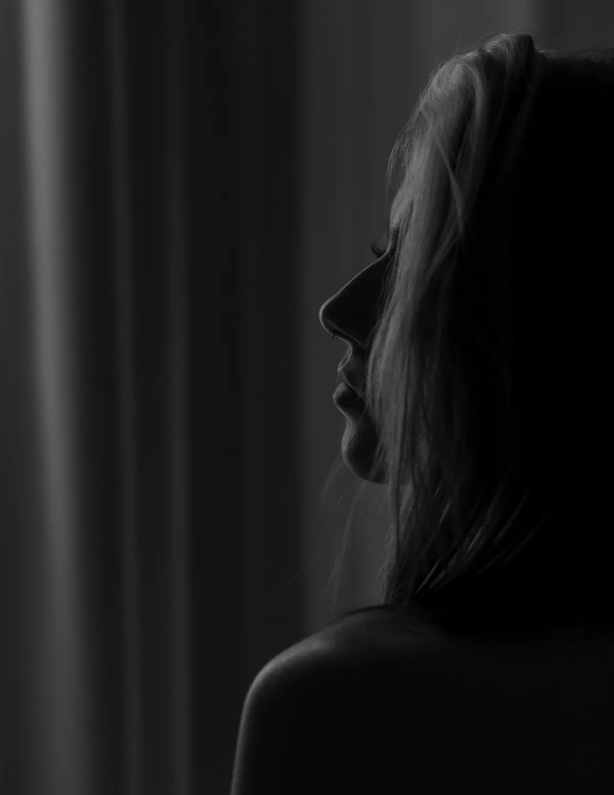 Moody profile portrait of Thaiss Windenberger standing beside a dark curtain