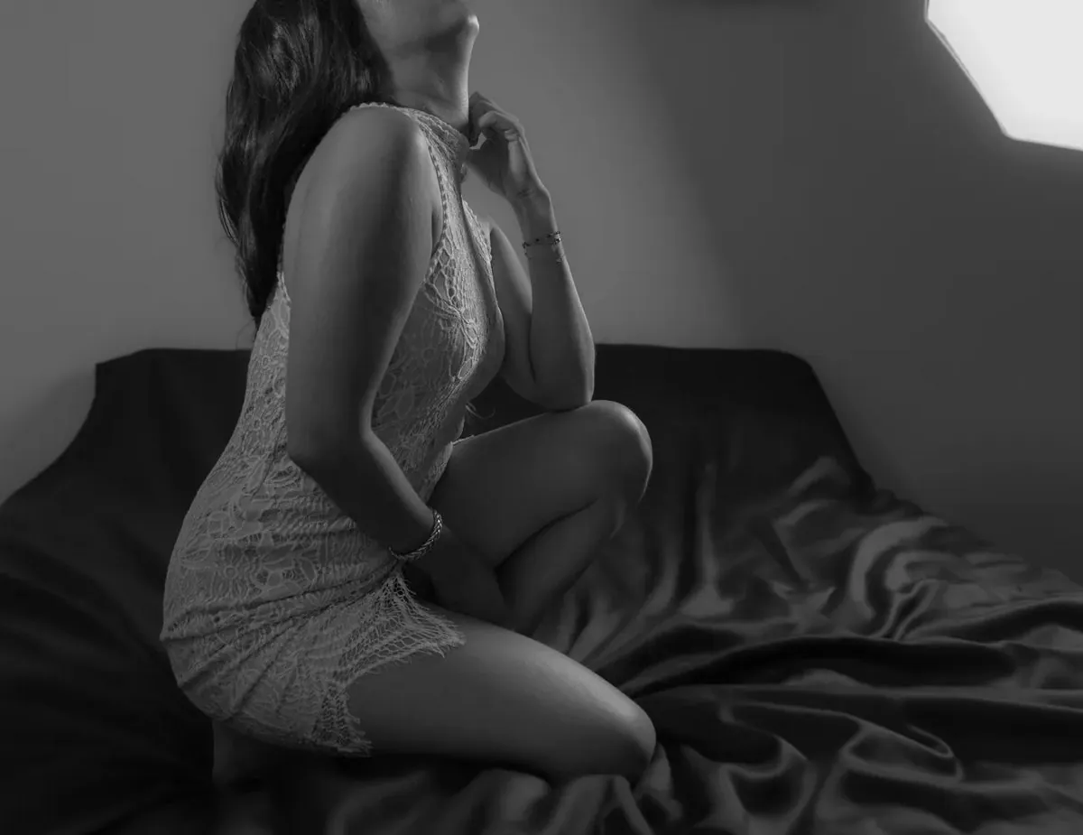 Black-and-white seated boudoir portrait of a woman wearing a soft white robe