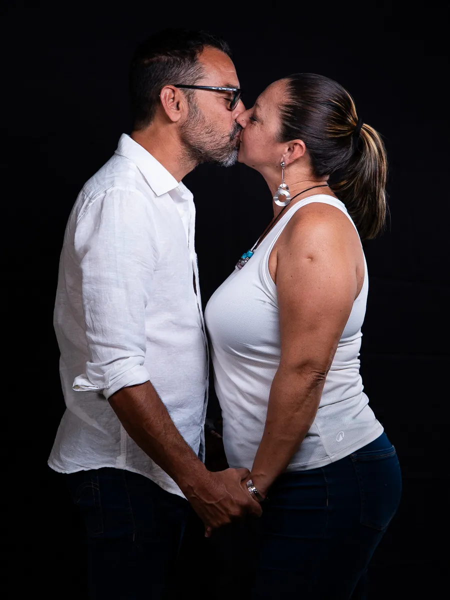 Couple kissing during a relaxed studio photoshoot against a dark background
