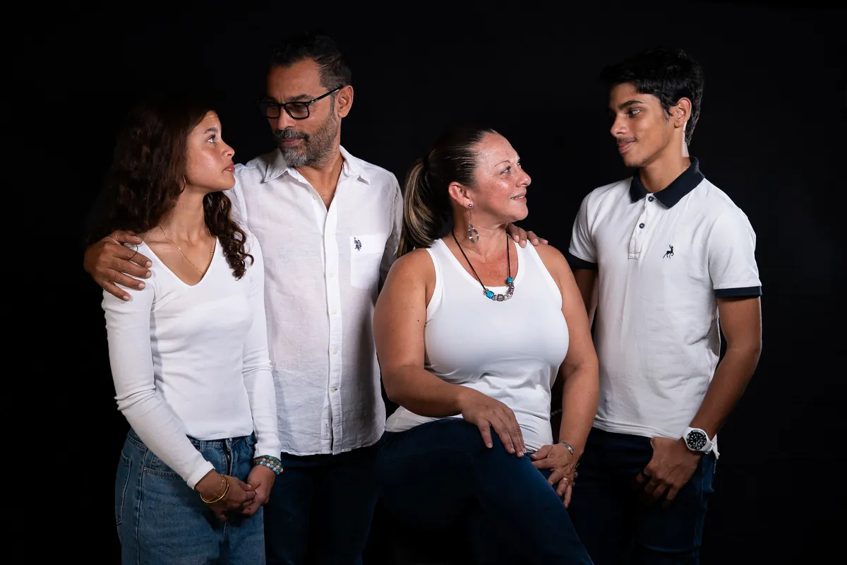 Family of four posing together during a relaxed studio photoshoot against a dark background