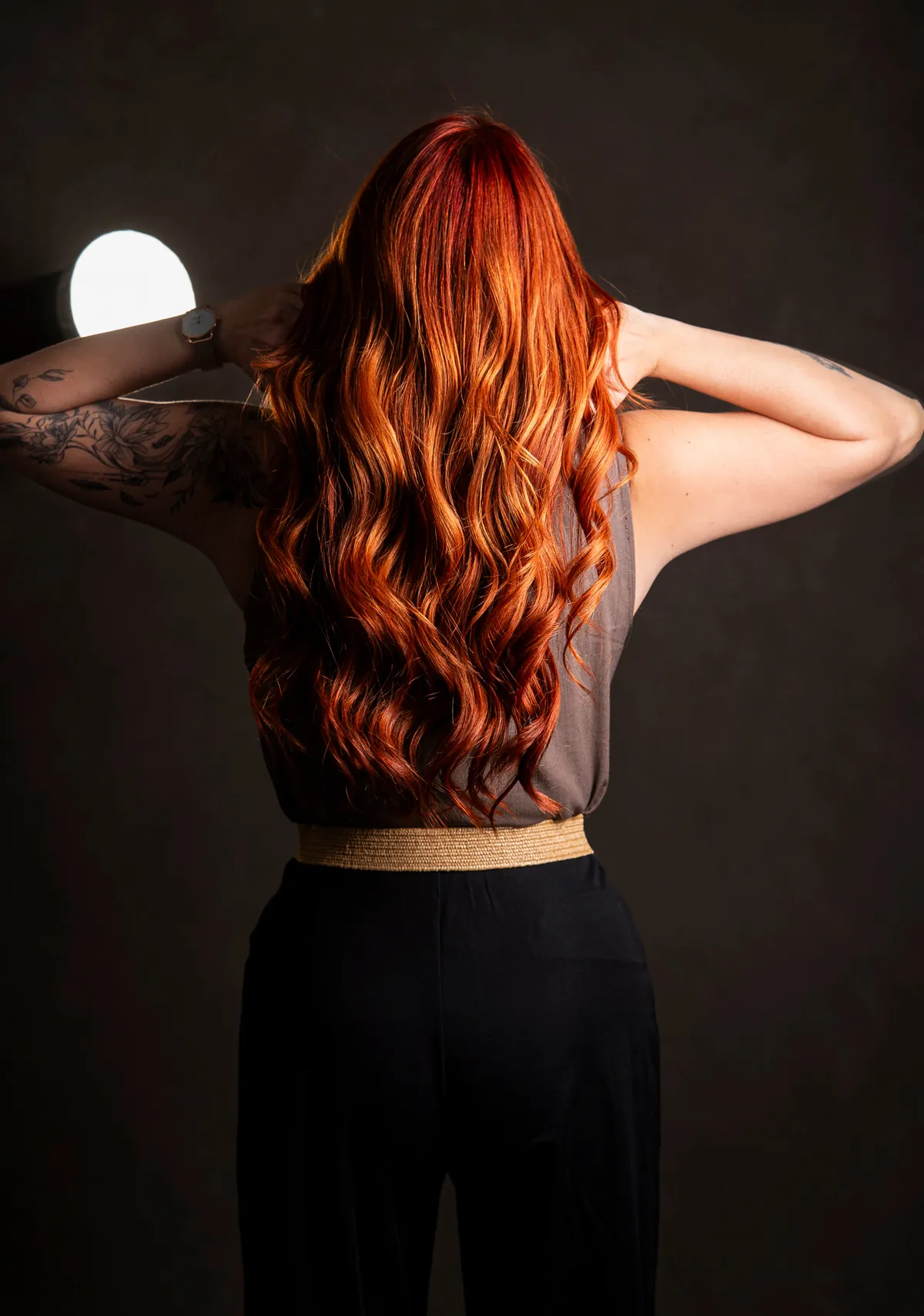 Back-view studio photograph of a red-haired woman with warm light defining her hair and shoulders