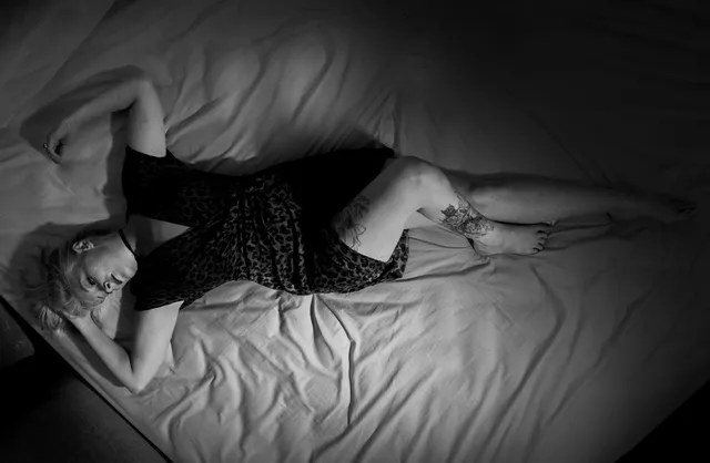 Black and white photography of tattooed & seductive female model lying in white sheet