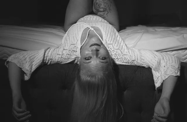 Sensual boudoir pose of girl lying on bed with legs raised and head upside down