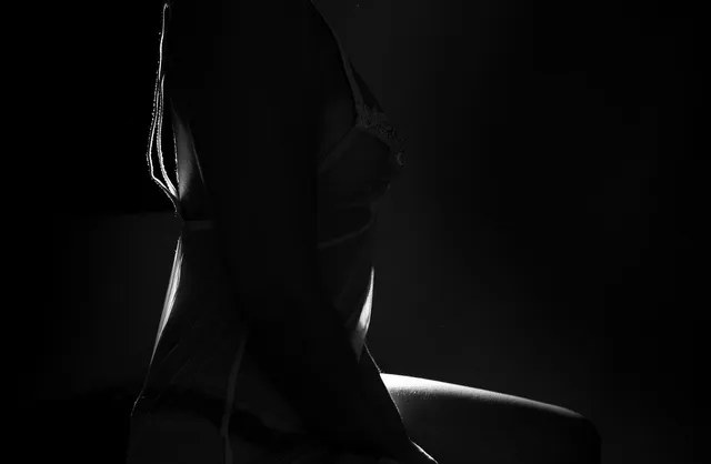 Photographie de nu artistique rétro-éclairée et à faible clé de la silhouette d'une fille assise et posant en lingerie