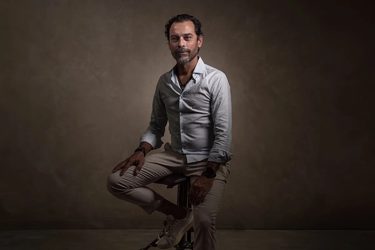 Finished studio portrait of a man seated against a textured background at Nude Art